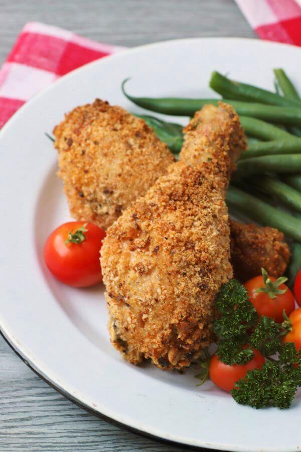 Two pieces of golden crispy oven baked chicken on a white plate with green beans and cherry tomatoes.