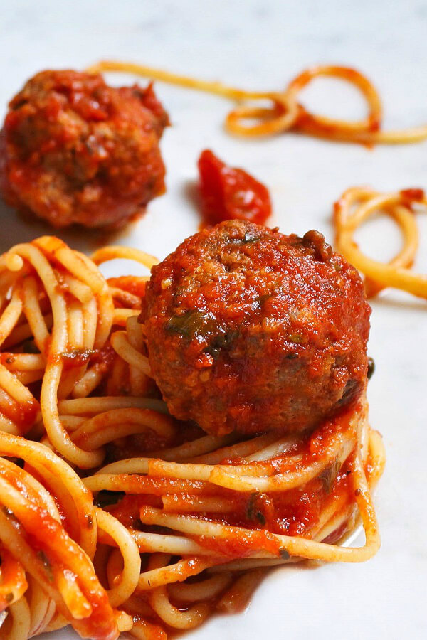 A group of saucy instant pot meatballs and coiled spaghetti on a white marble background.