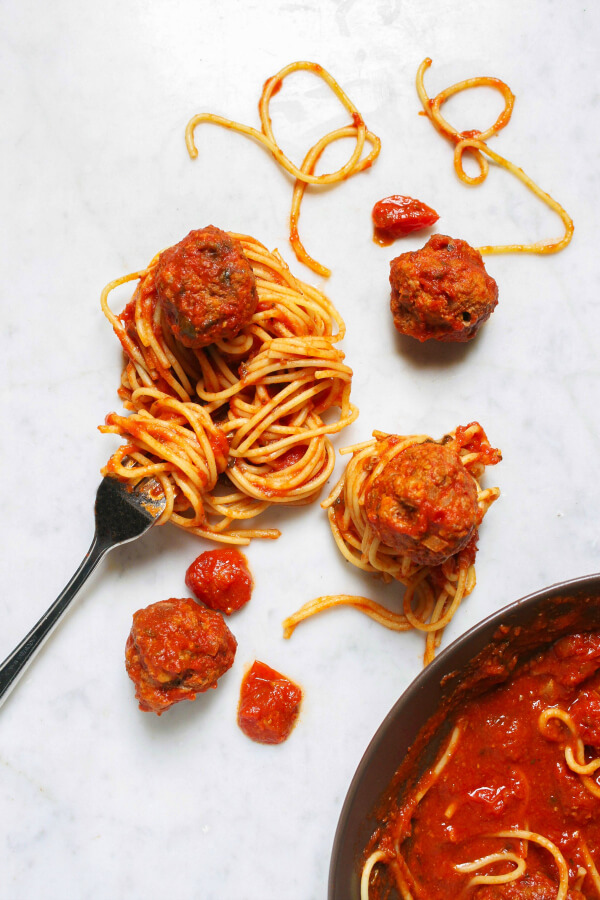 A group of saucy instant pot meatballs and coiled spaghetti on a white marble background.