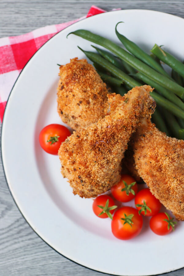 Three pieces of golden crispy oven baked chicken on a white plate with green beans and cherry tomatoes.