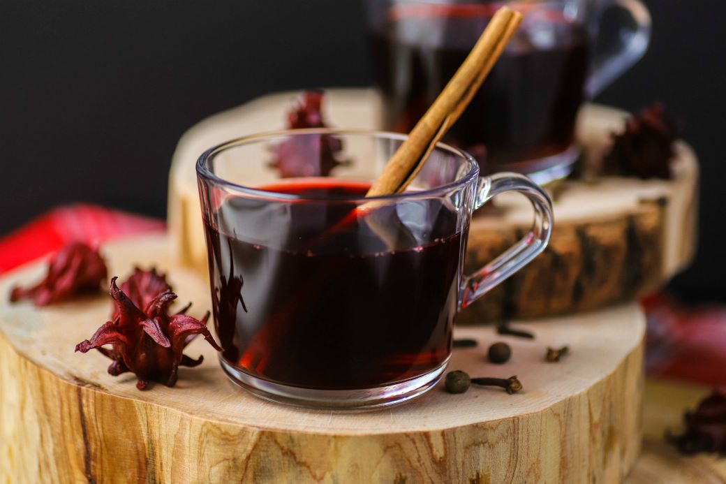 A clear glass cup filled with red sorrel drink and a cinnamon stick.