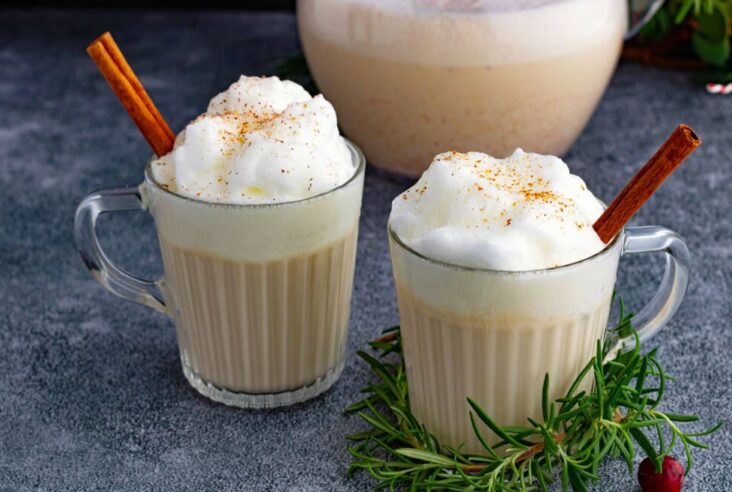 Two glass mugs filled with creamy eggnog topped with foam and grated nutmeg.