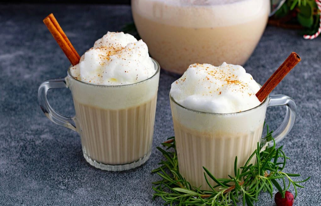 Two glass mugs filled with creamy eggnog topped with foam and grated nutmeg.