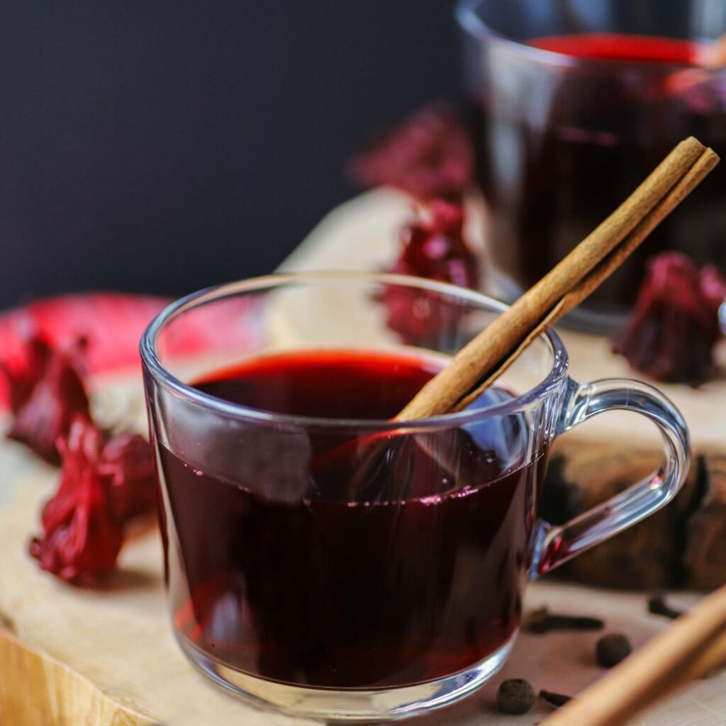 A clear glass cup filled with red sorrel drink and a cinnamon stick.