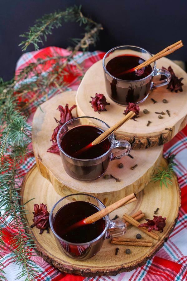 Three clear glass cups filled with red sorrel drink and a cinnamon stick.