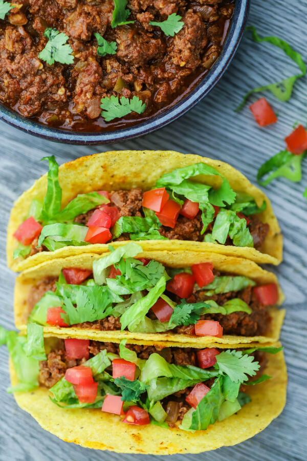 Three filled hard shell tacos and a bowl of crockpot taco meat.