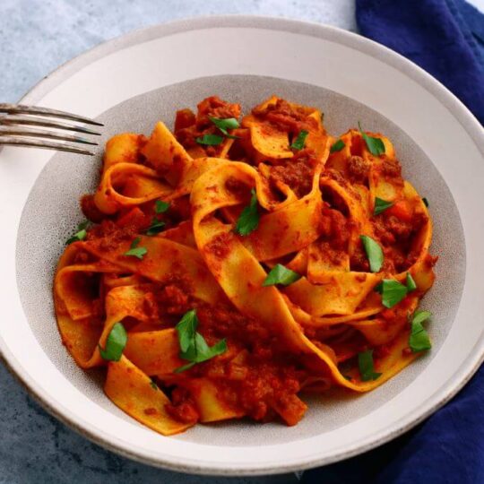 A bowl of wide flat papardelle noodles covered in bright red Bolognese.