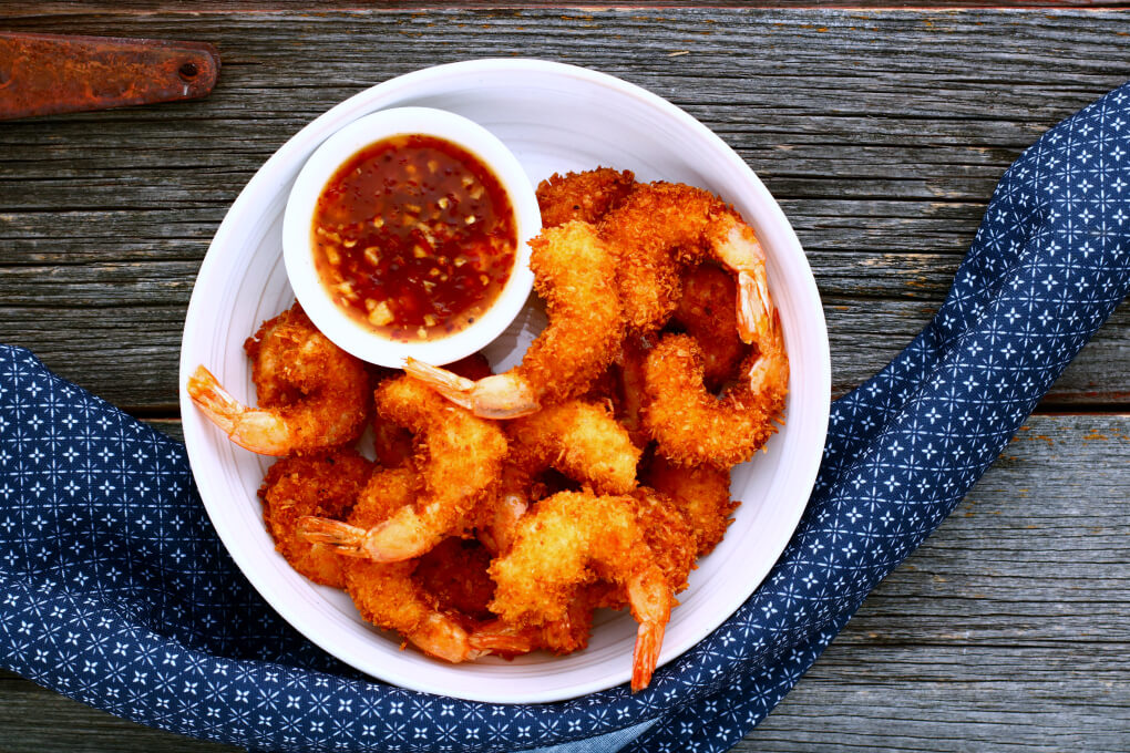 A bowl of crispy golden fried shrimp and red dipping sauce.