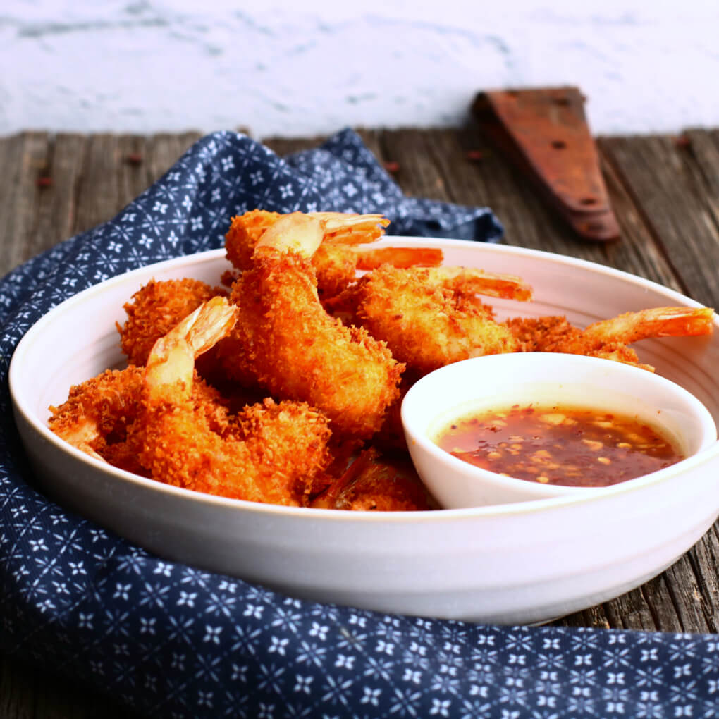 A bowl of crispy golden fried shrimp and red dipping sauce.