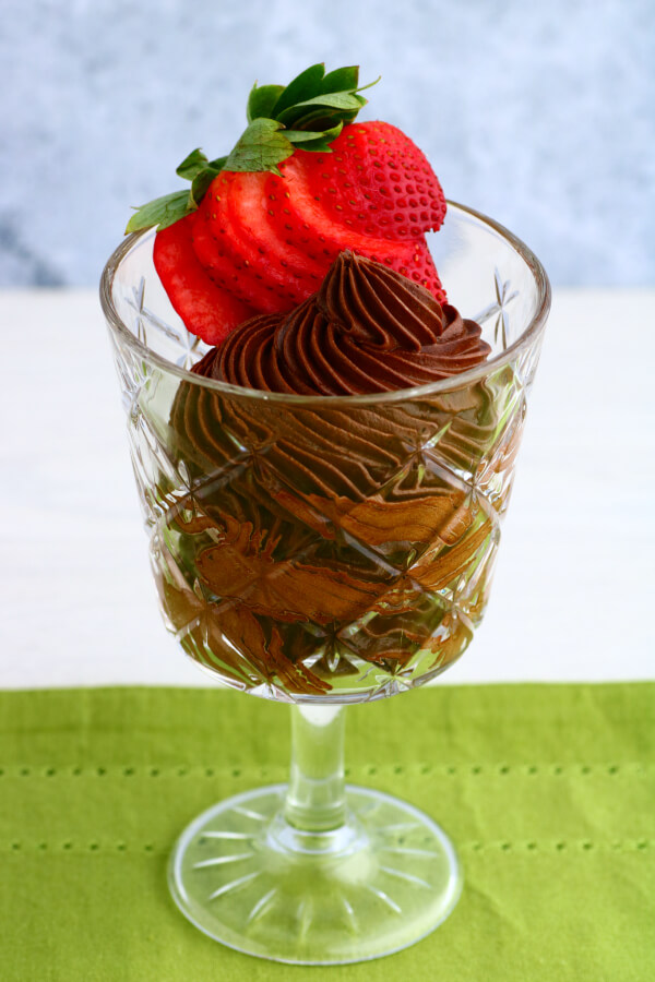 A crystal glass filled with dark chocolate avocado mousse topped with a strawberry.