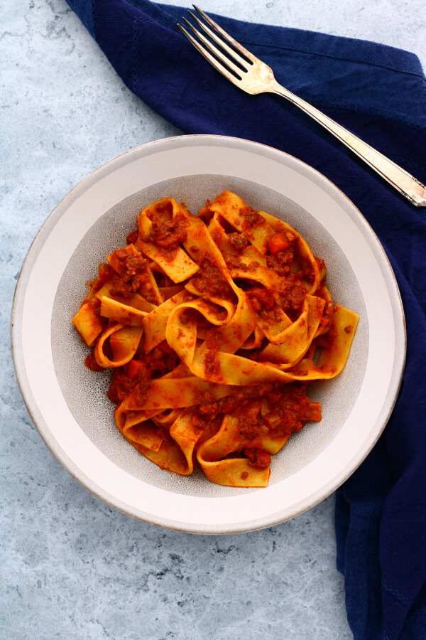 A bowl of wide flat papardelle noodles covered in bright red Bolognese.