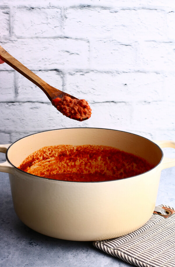 A wooden spoon holds bright red rich meat sauce over a pot of sauce.
