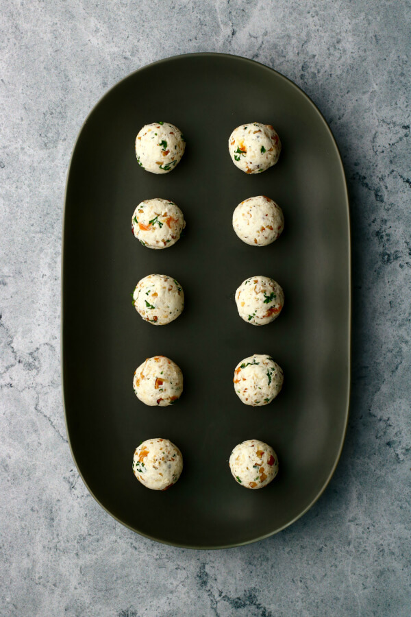 Goat cheese balls lined up on a dark platter before frying.