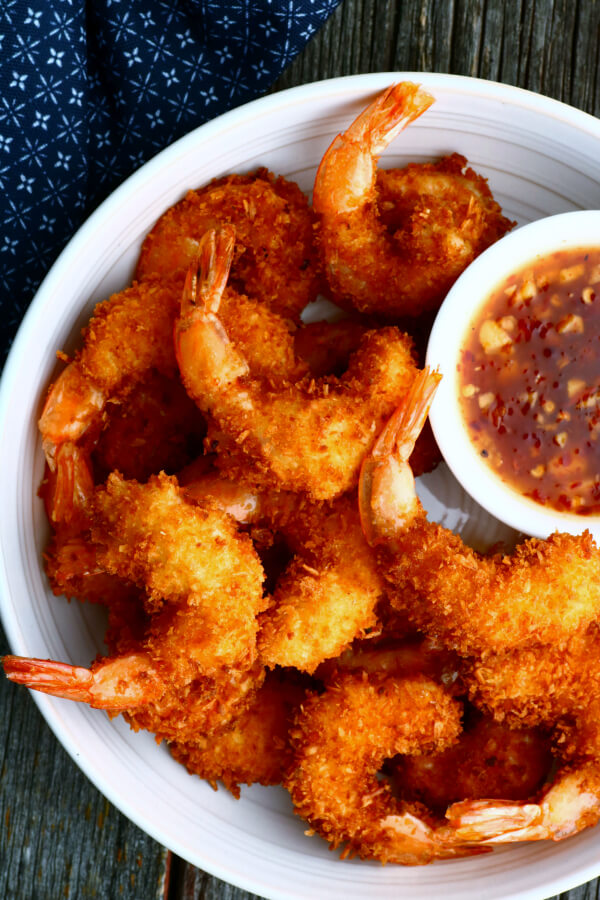 A bowl of crispy golden fried shrimp and red dipping sauce.