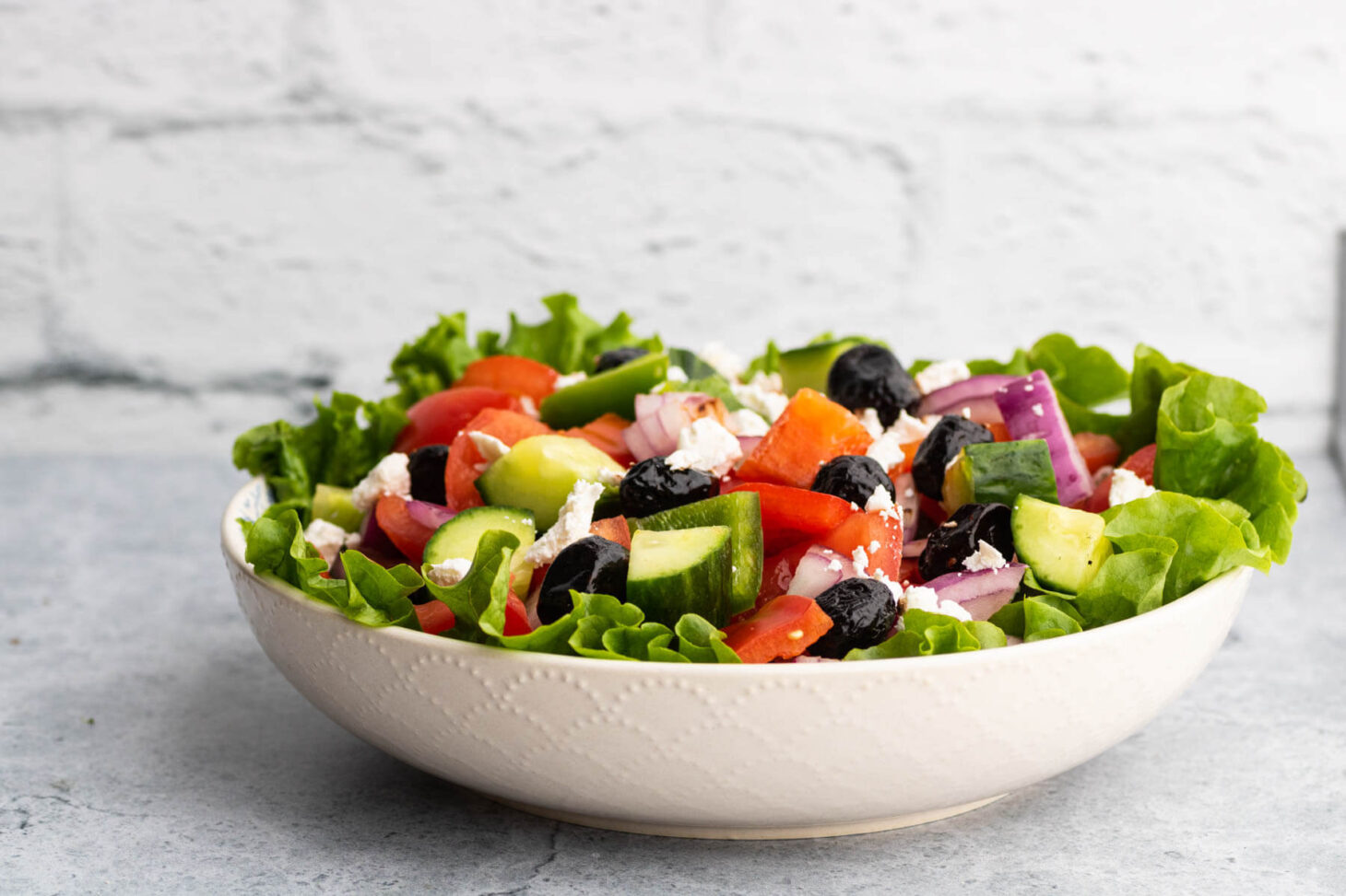 A white bowl filled with chopped tomatoes, peppers, red onions, cucumbers, black olives, and feta cheese.