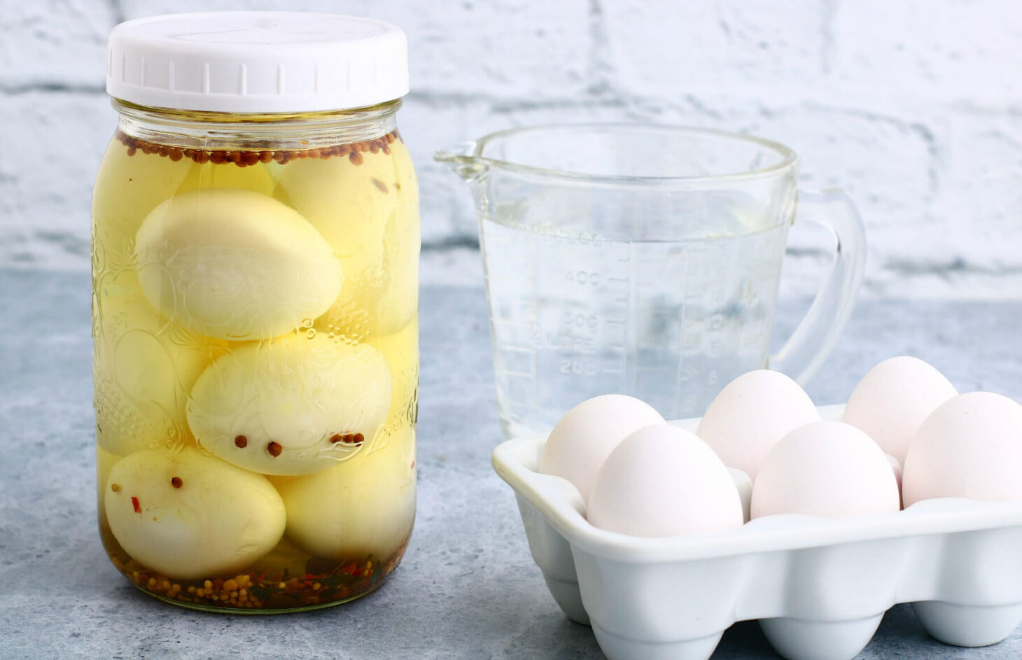 Hard boiled Pickled eggs in a jar with a tray of eggs nearby.