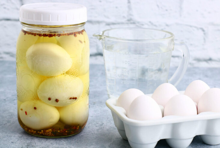 Hard boiled Pickled eggs in a jar with a tray of eggs nearby.