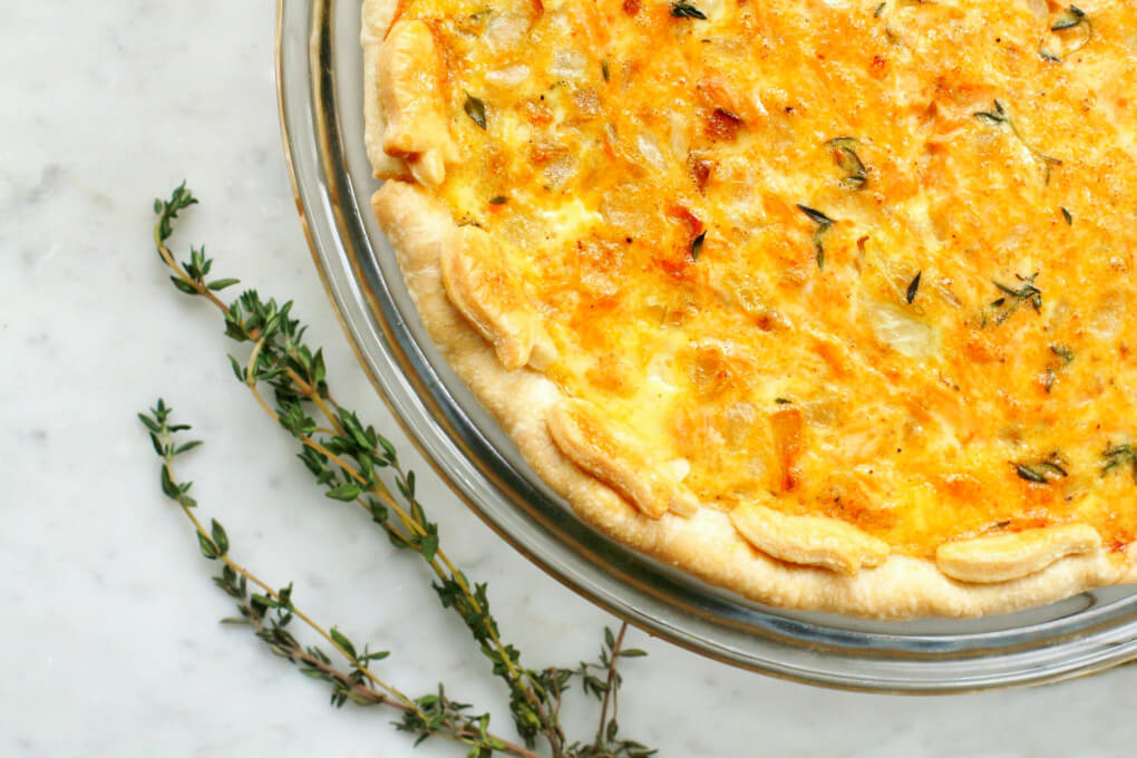 A golden baked quiche on white marble surrounded by fresh thyme.