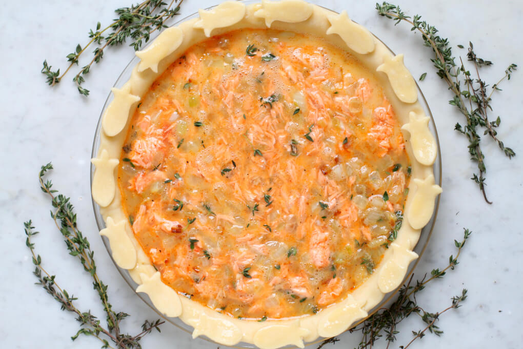 An unbaked pie shell filled with pink canned fish, beaten eggs, and fresh thyme.
