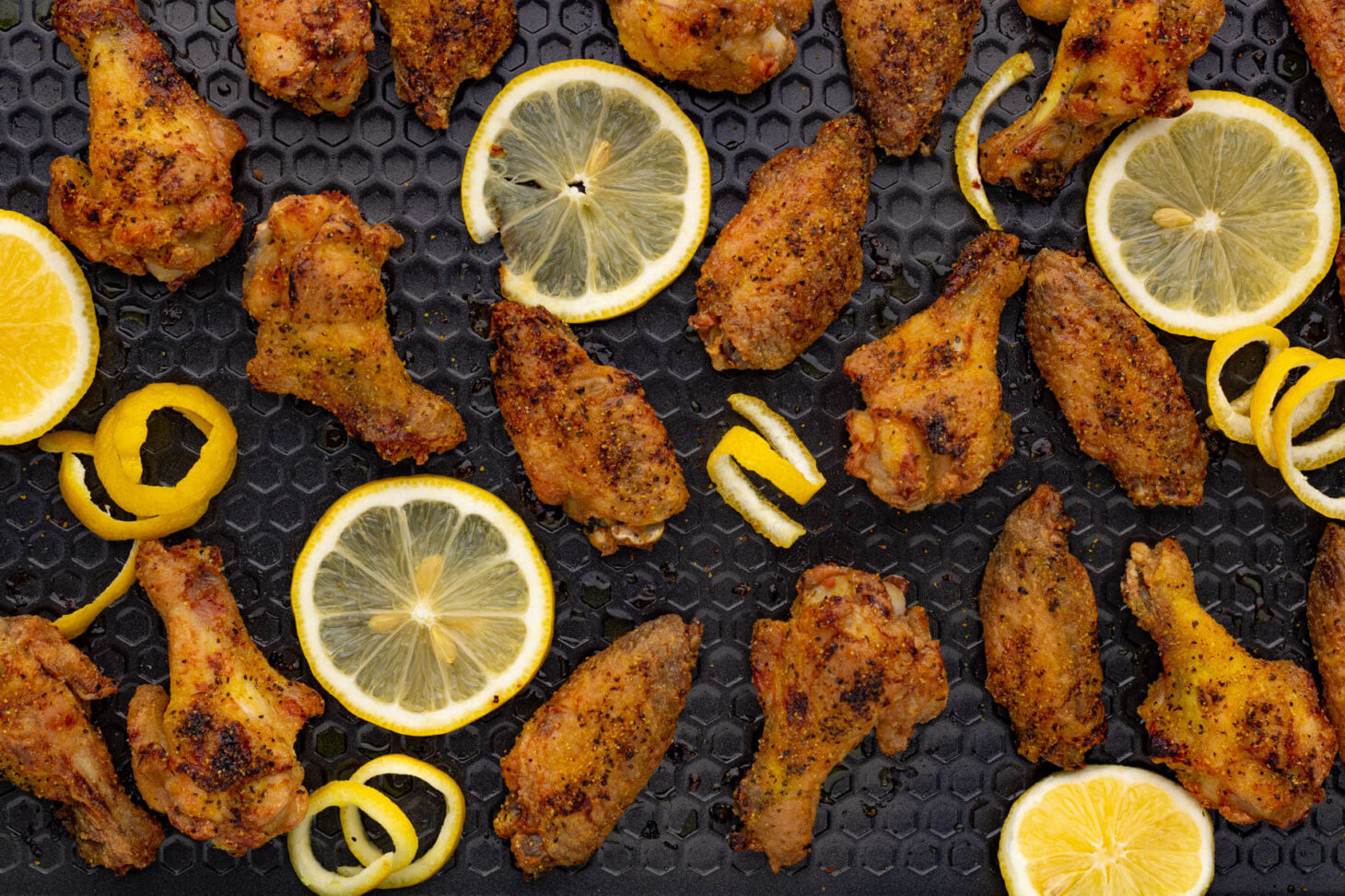 A baking sheet filled with crispy baked lemon pepper wings and lemon slices.