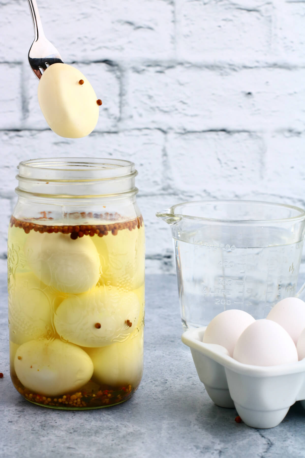 A fork holding a hard boiled pickled egg over an open jar of eggs.