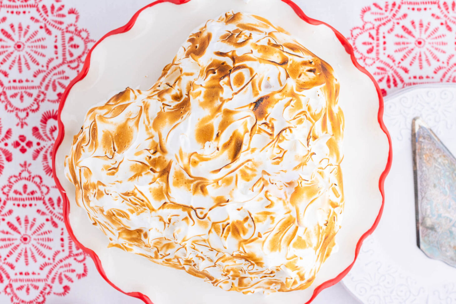 A heart shaped Baked Alaska covered in caramelized meringue on a red rimmed plate.