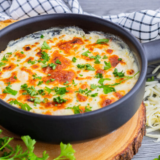 A cheesy golden baked Shrimp scampi dip in a black baking dish.