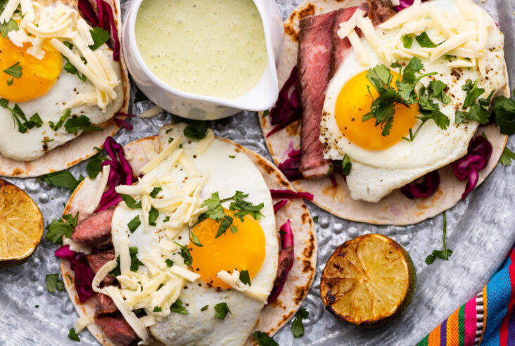 Three steak and egg tacos topped with cheese and cilantro.
