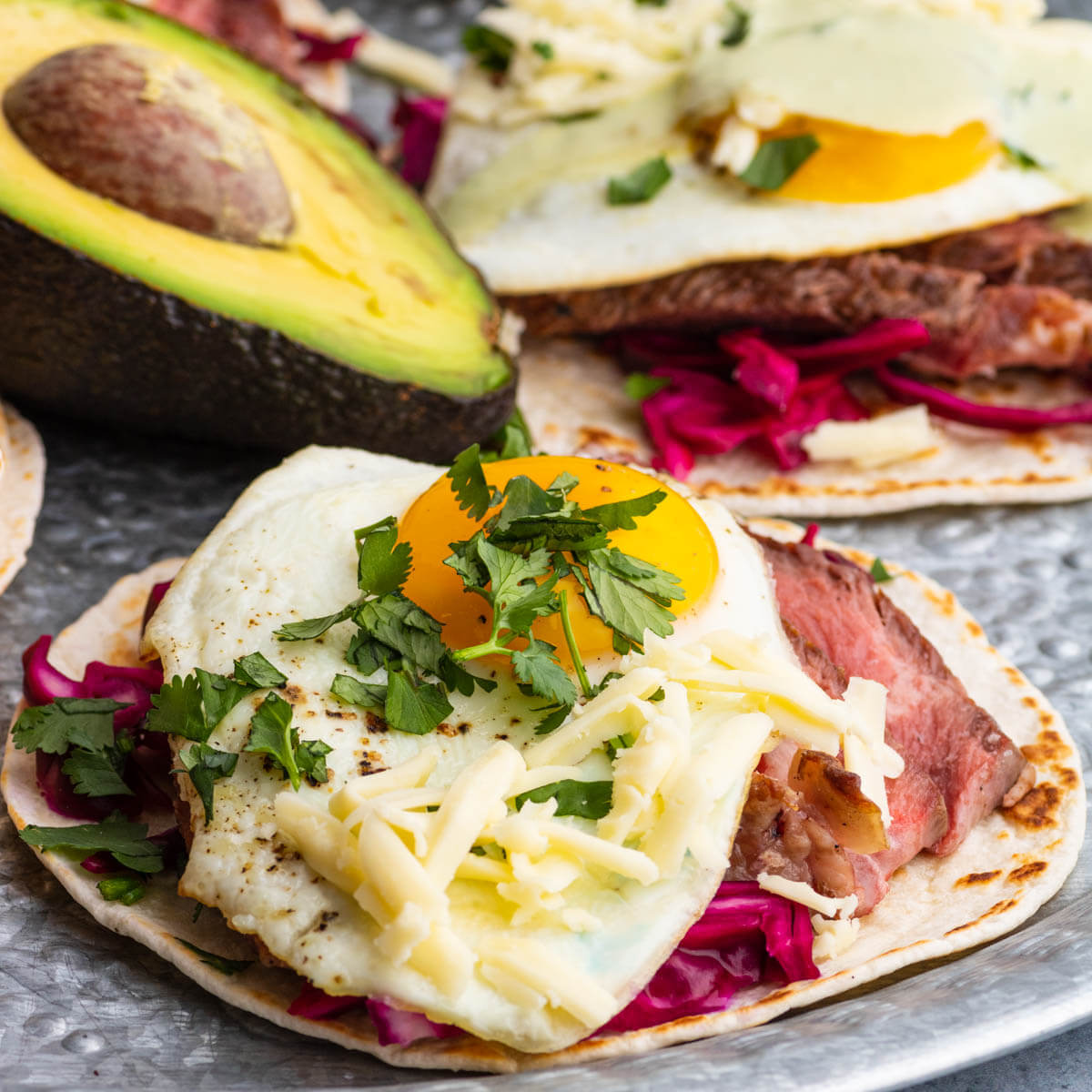 A steak taco topped with sunny side up fried egg, grated cheese, and cilantro.