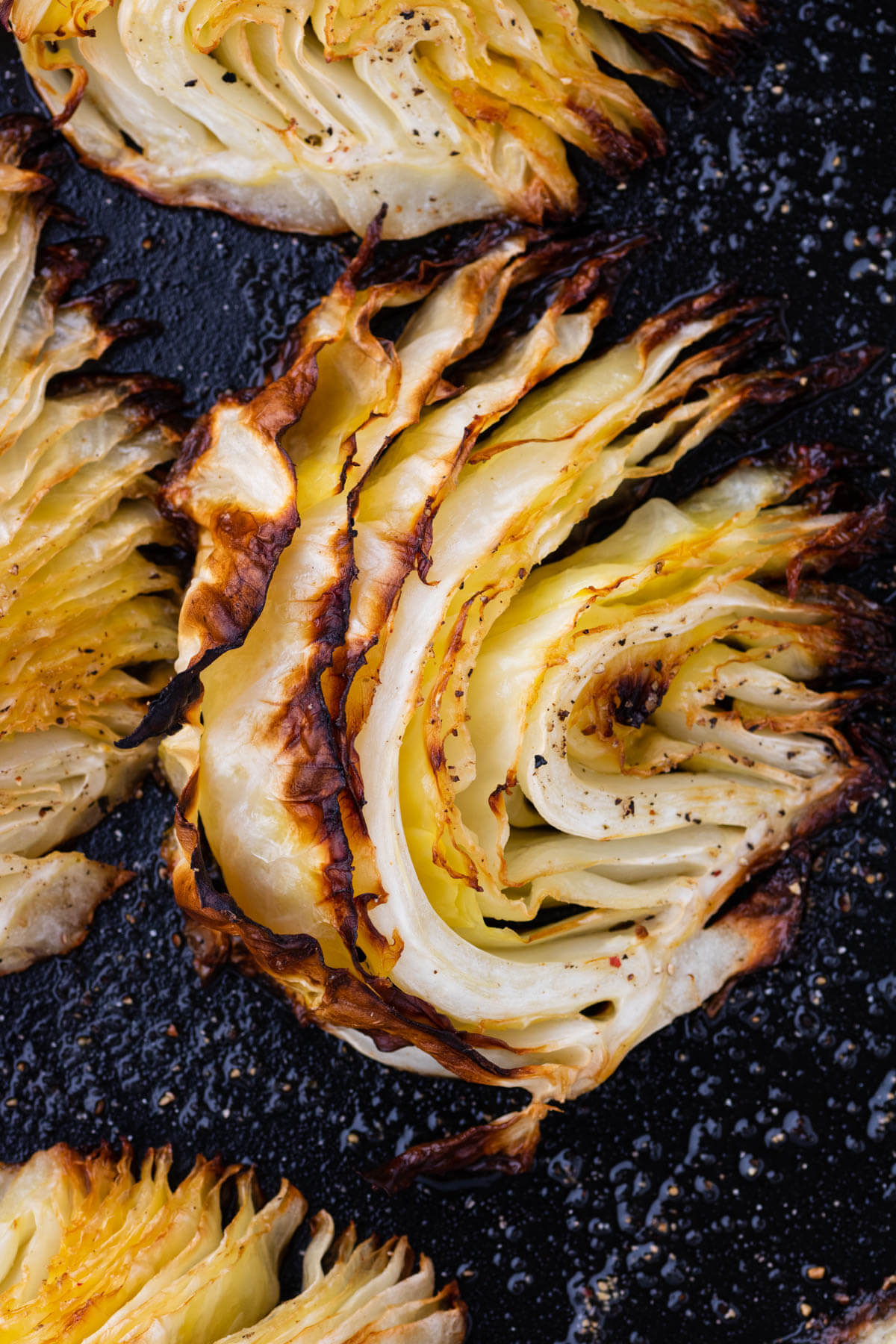 A wedge of Roasted Cabbage in a dark roasting pan.