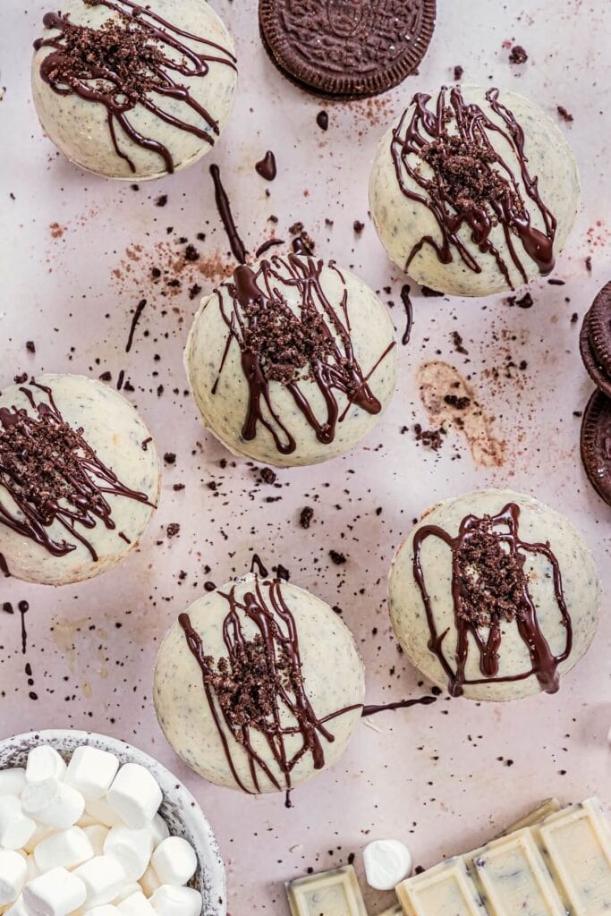 A tray of chocolate bombs decorated with cookie crumbs and dark chocolate drizzle.