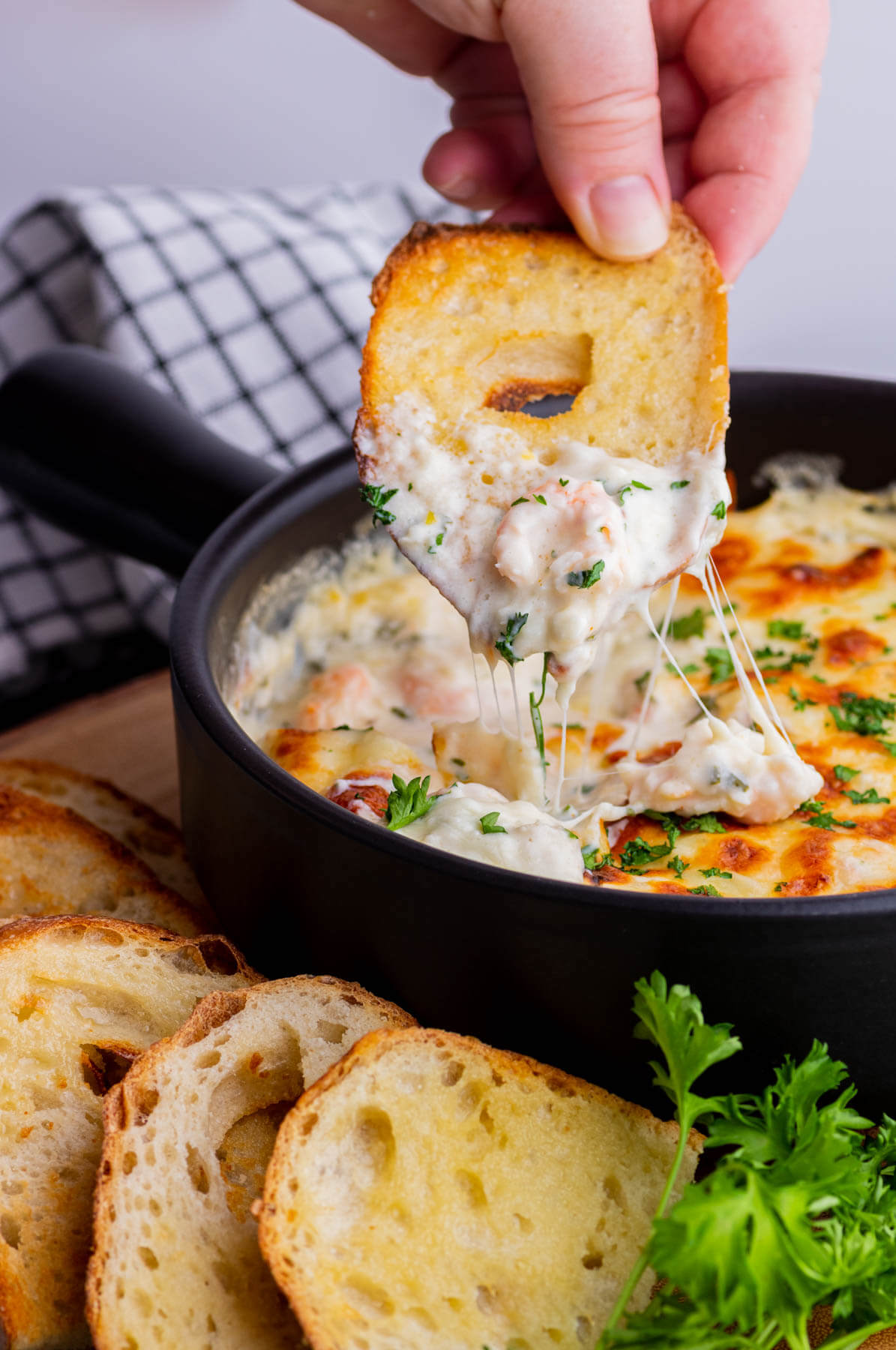 A slice of baguette being dipped into cheesy shrimp scampi dip.