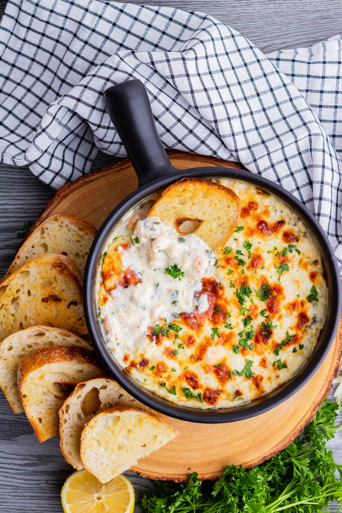 A slice of baguette dipped into cheesy shrimp scampi dip.