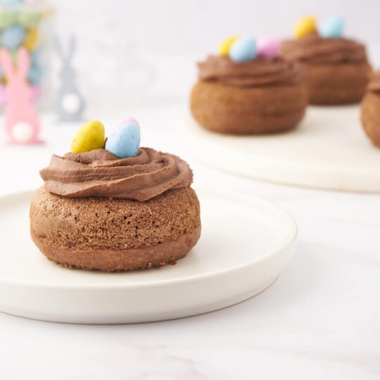 Chocolate baked donuts decorated as Easter Nests filled with Mini Eggs in an Easter table setting.