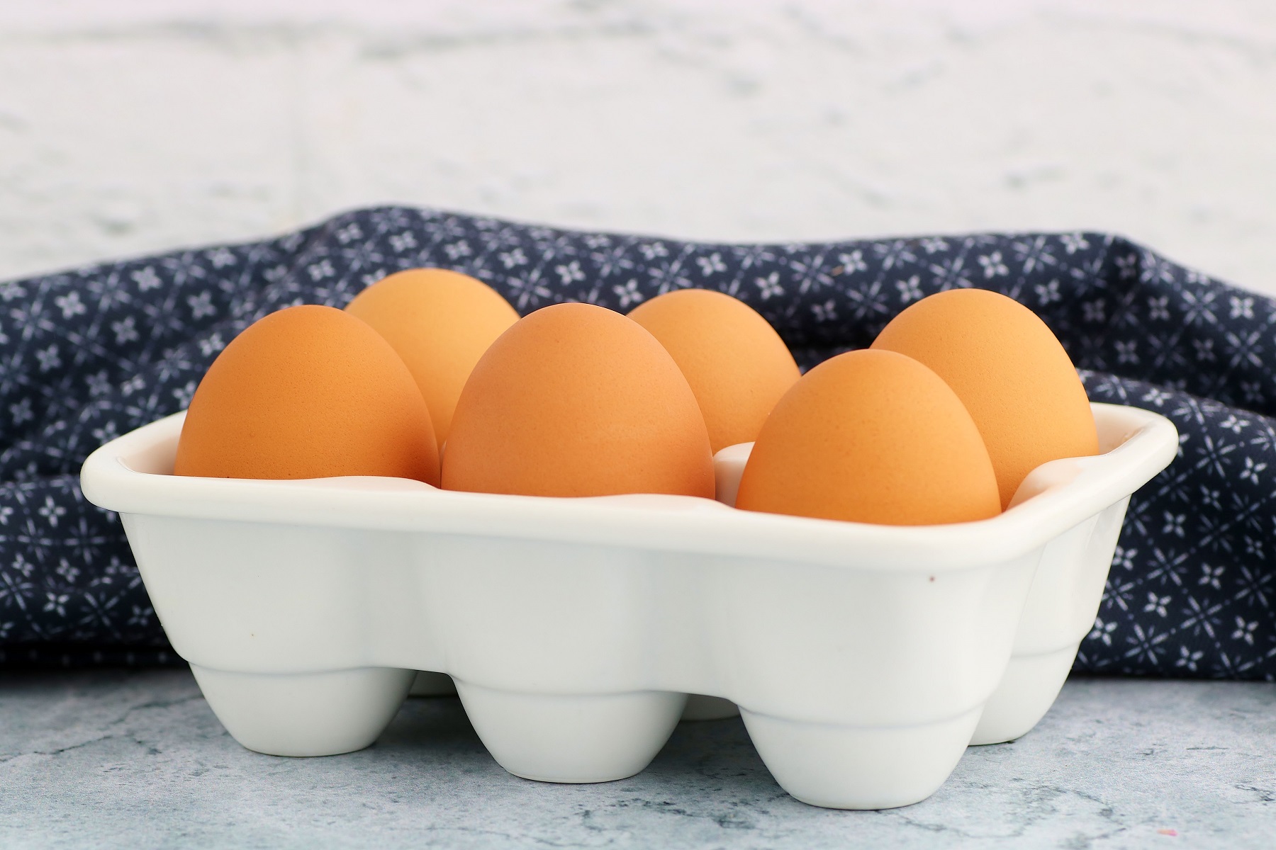 A white ceramic egg carton holding six brown eggs.