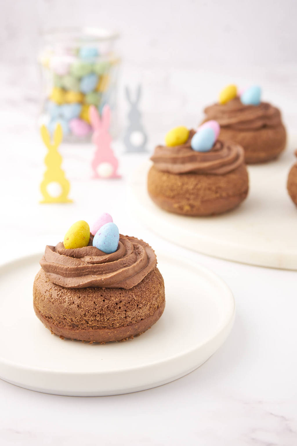 Chocolate baked donuts decorated as Easter Nests filled with Mini Eggs in an Easter table setting.