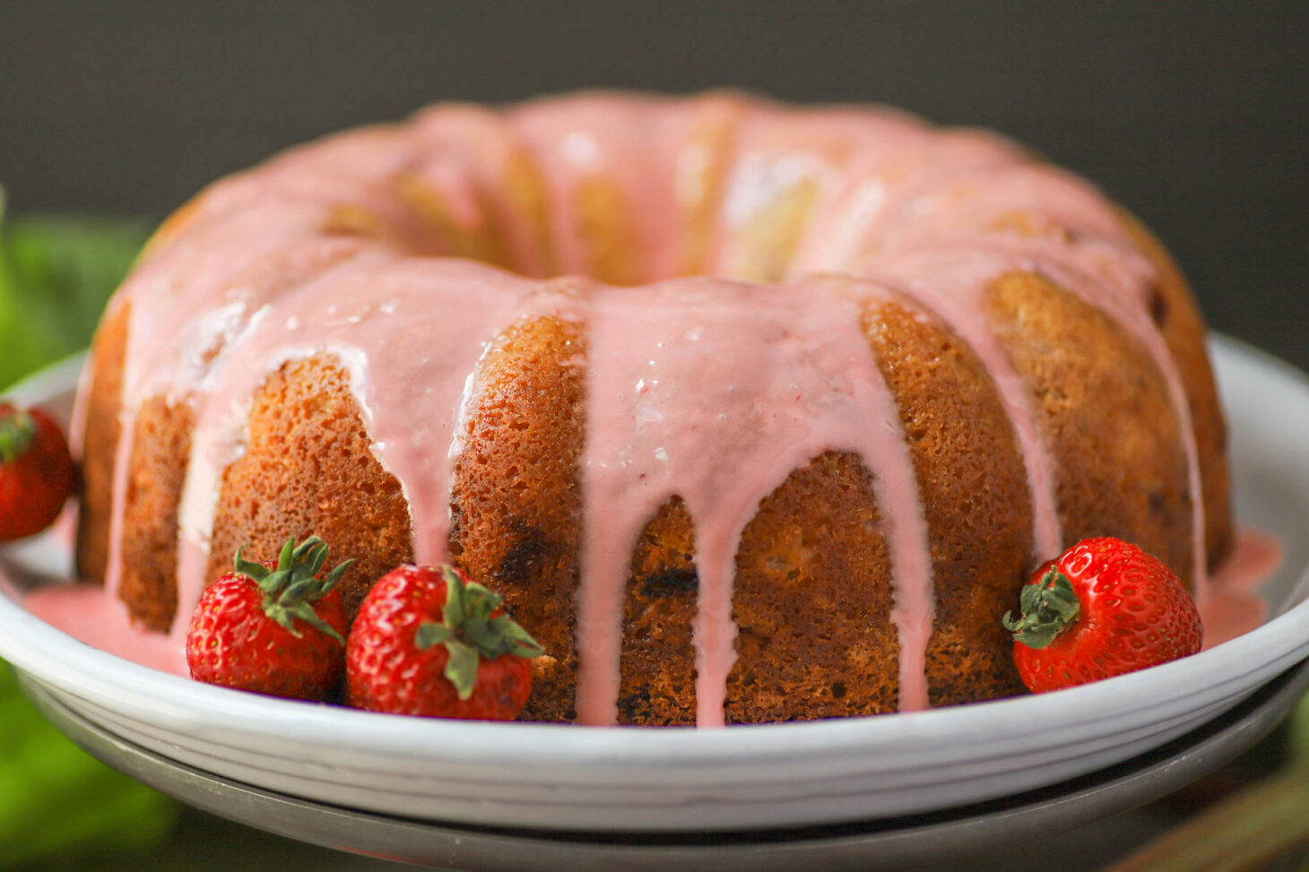 A golden baked bundt cake topped with pink glaze.