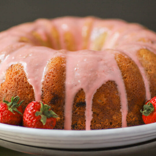 A golden baked bundt cake topped with pink glaze.