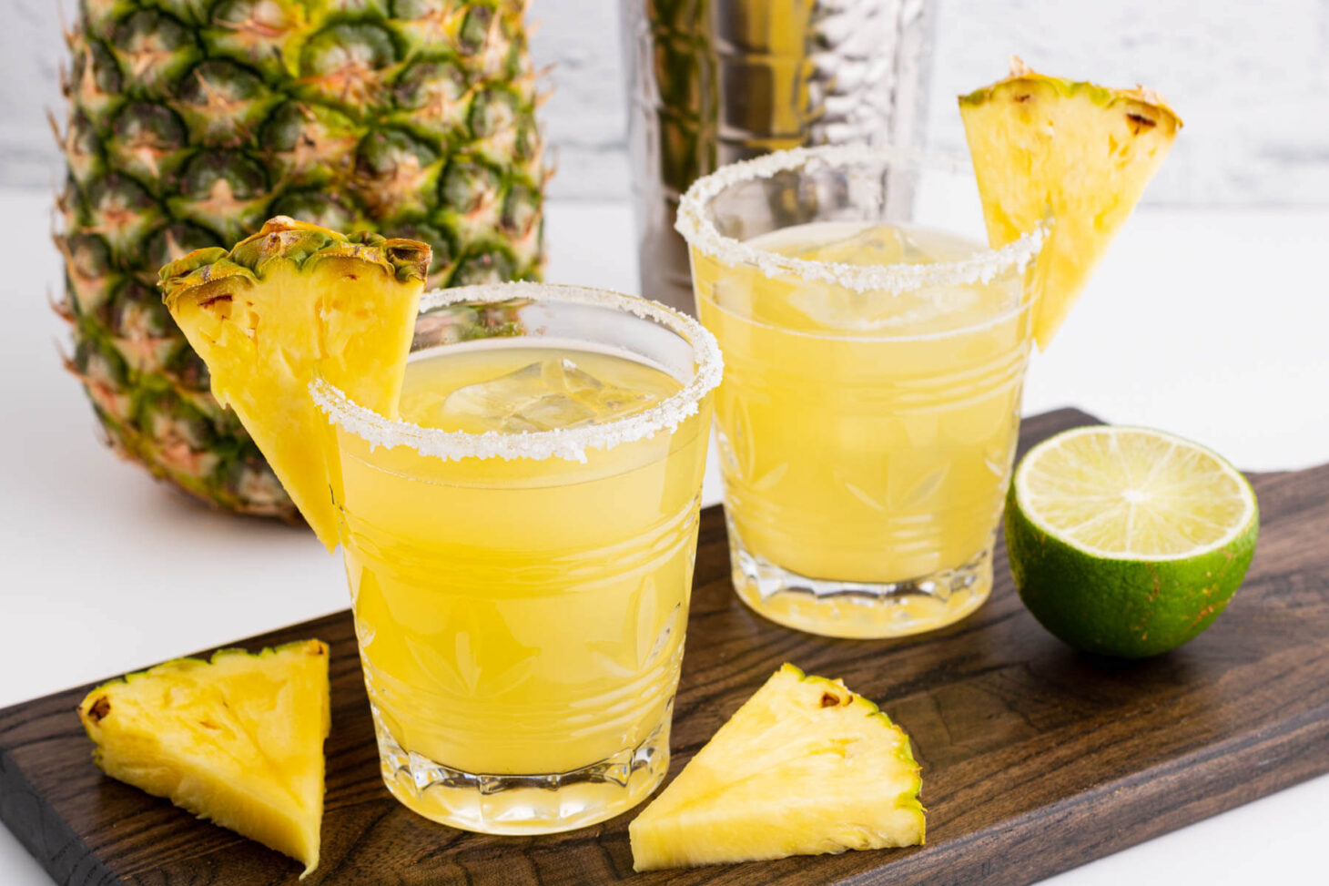 Two rimmed rocks glasses filled with ice and pineapple margarita. Garnished with a slice of pineapple.