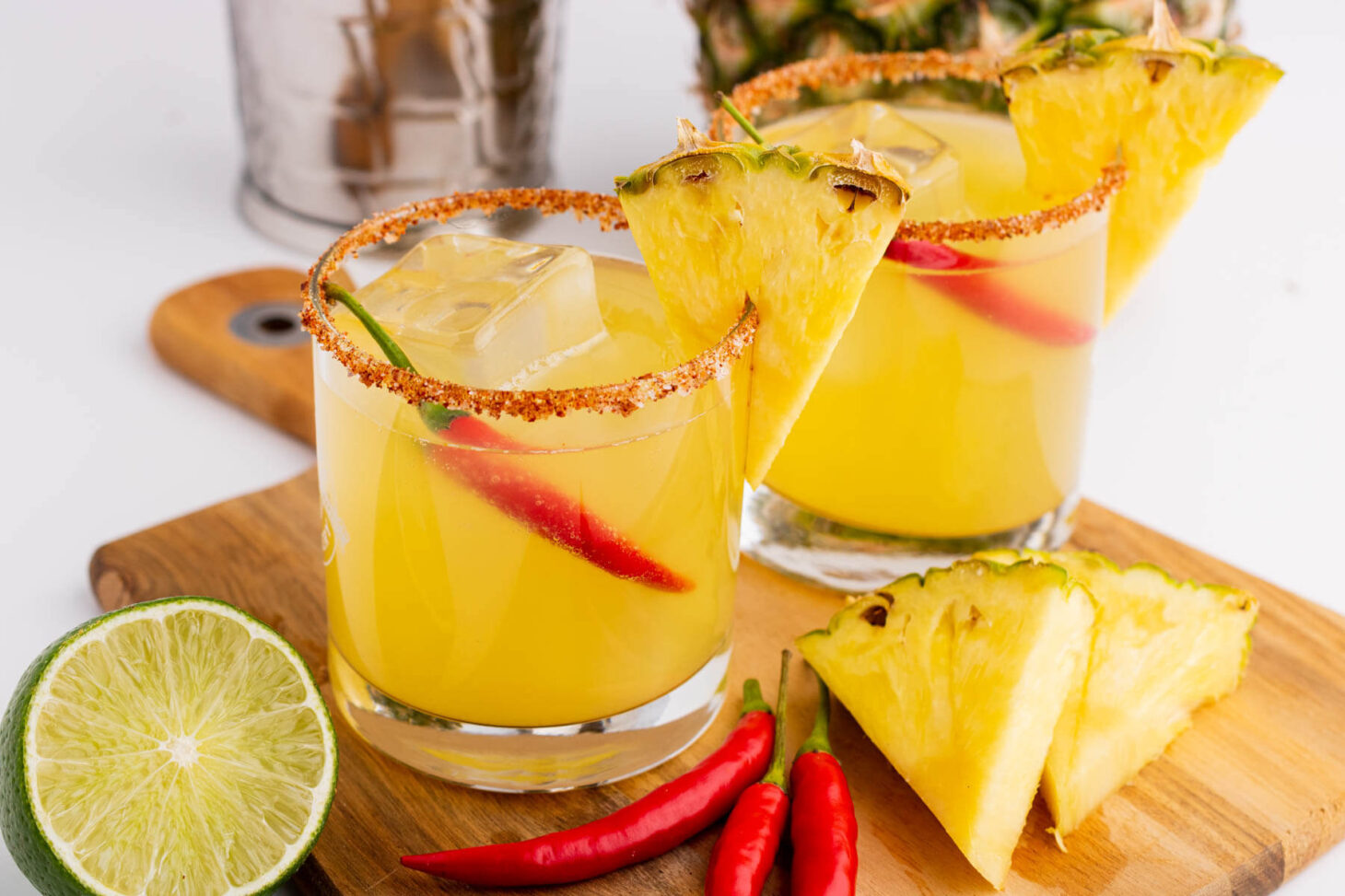 Two Spicy Pineapple Margaritas in red rimmed rocks glasses garnished with a wedge of pineapple and red chili pepper.