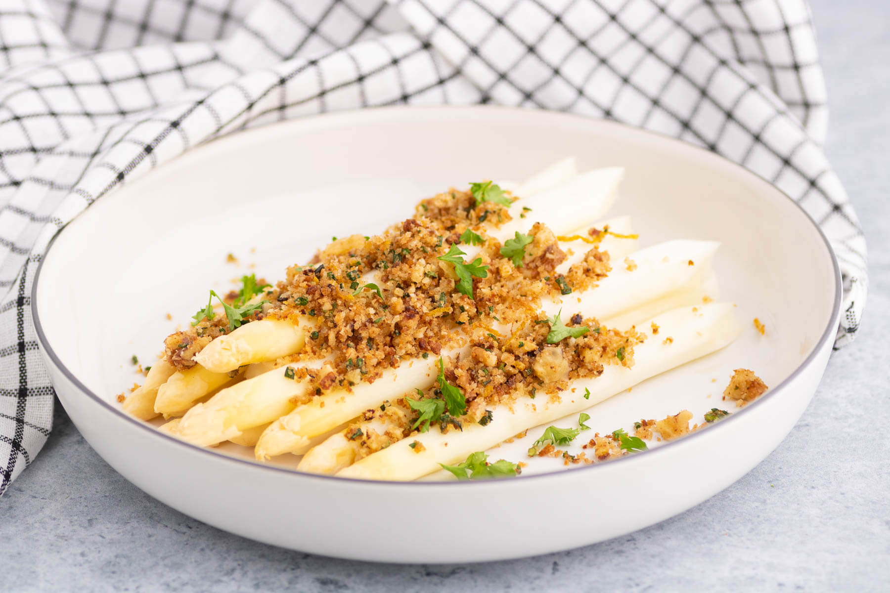 A plate of steamed white asparagus covered in golden pangrattato and herbs.