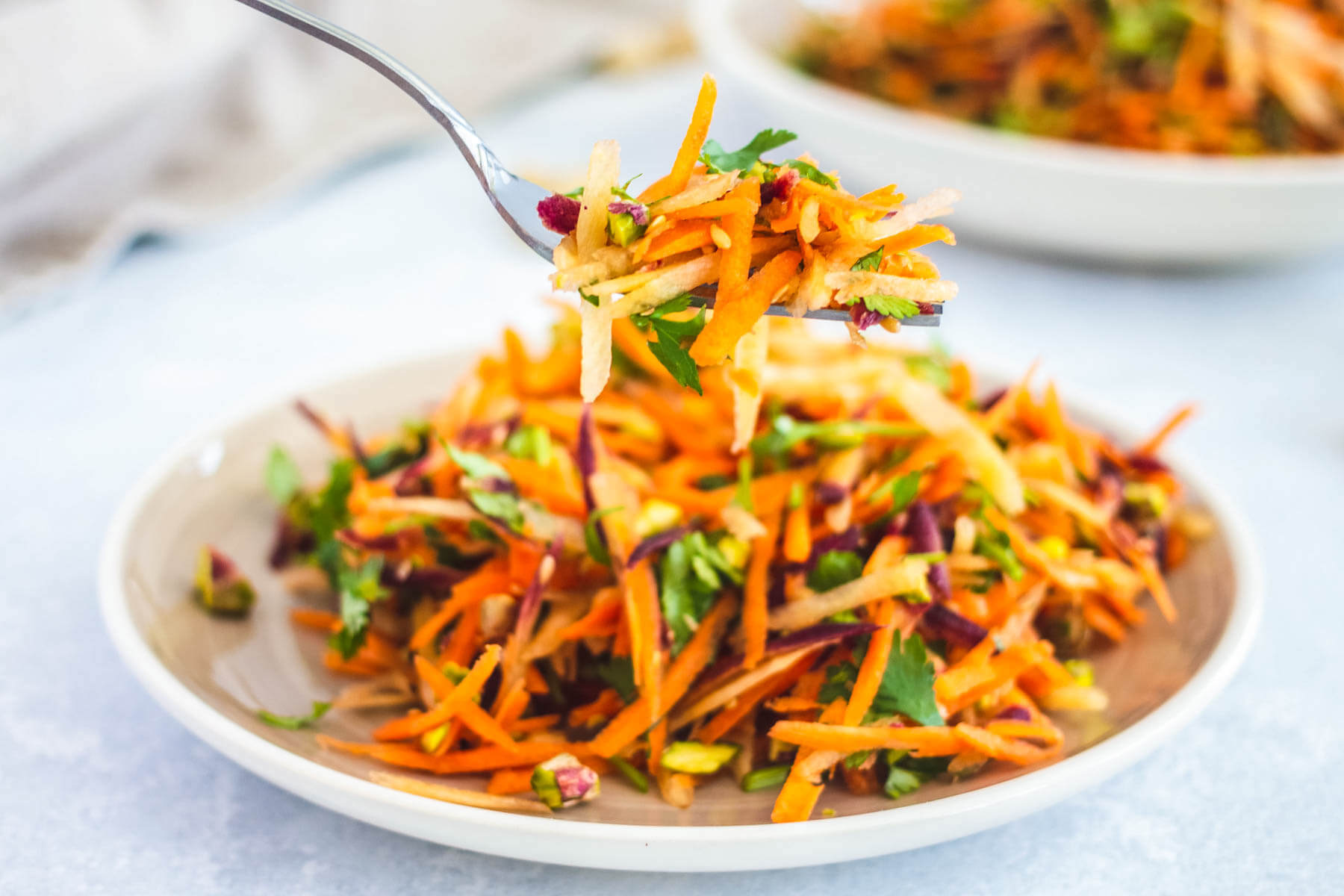 A fork holding colourful carrot salad over a bowl of salad.