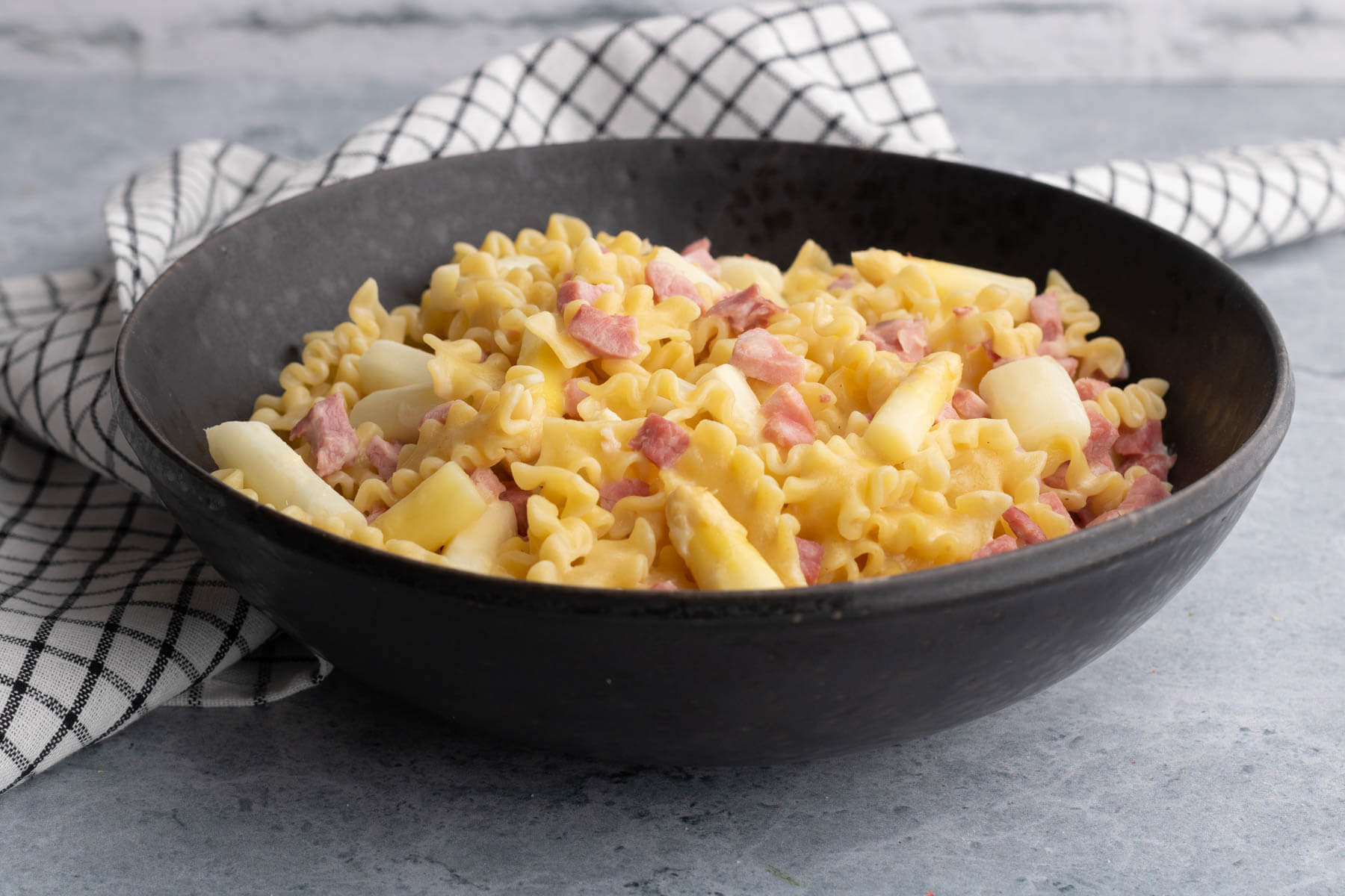 A bowl of lemon butter pasta with ham and white asparagus.