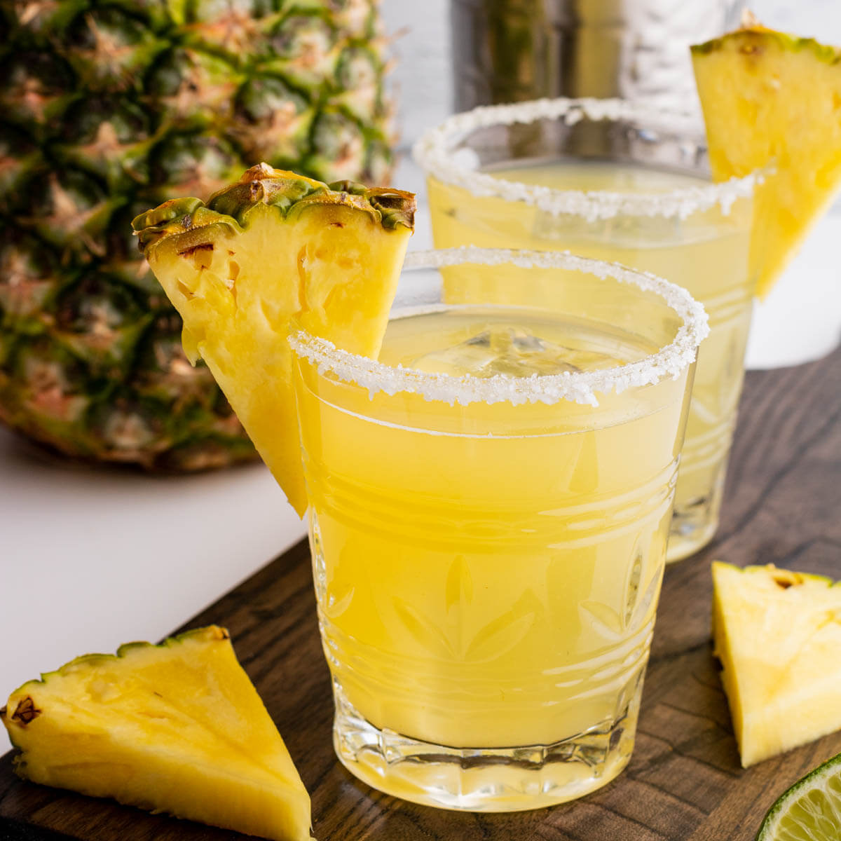 A rimmed rocks glass filled with ice and pineapple margarita. Garnished with a slice of pineapple.