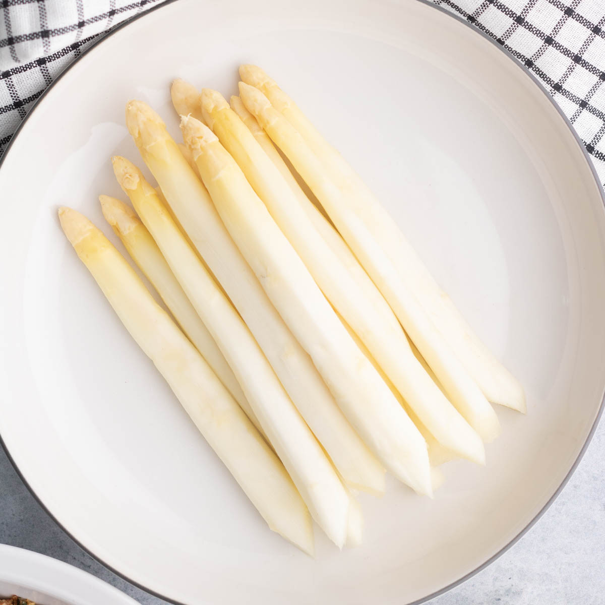 A white plate with a bunch of steamed white asparagus.