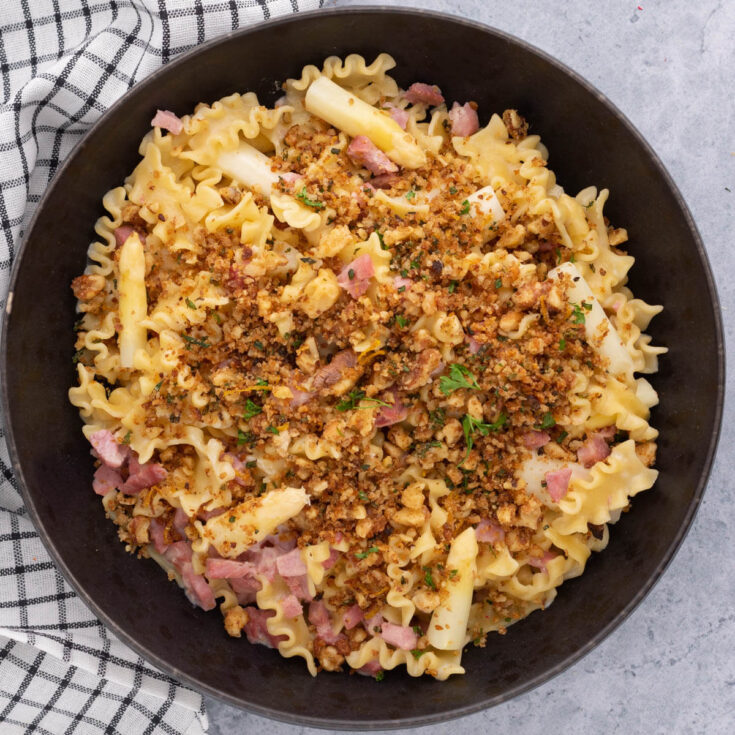 A bowl of lemon butter pasta with ham and white asparagus topped with golden herbed bread crumbs.