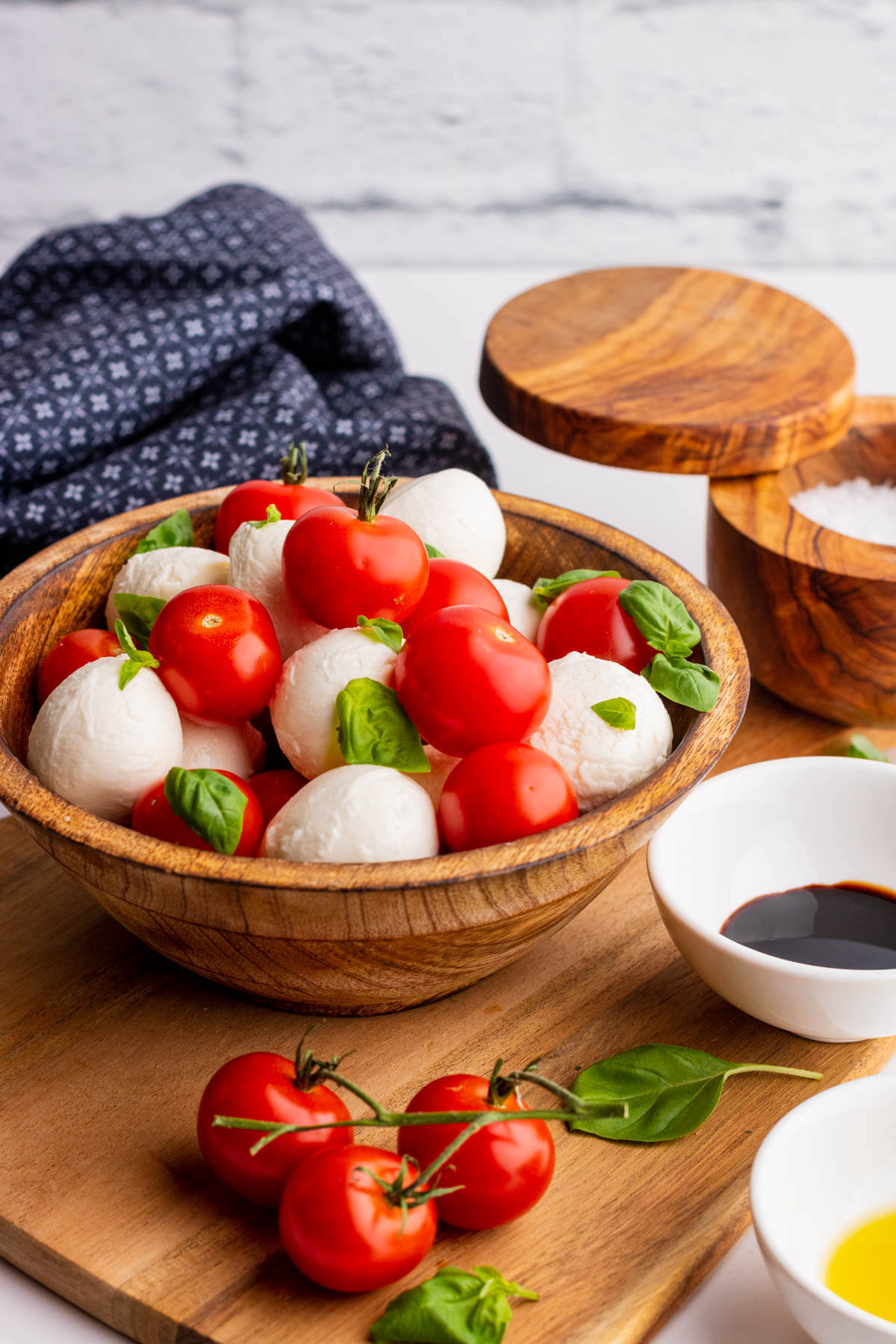 A wooden bowl filled with bright red cherry tomatoes, white mozzarella balls and green basil drizzled with olive oil and balsamic reduction.