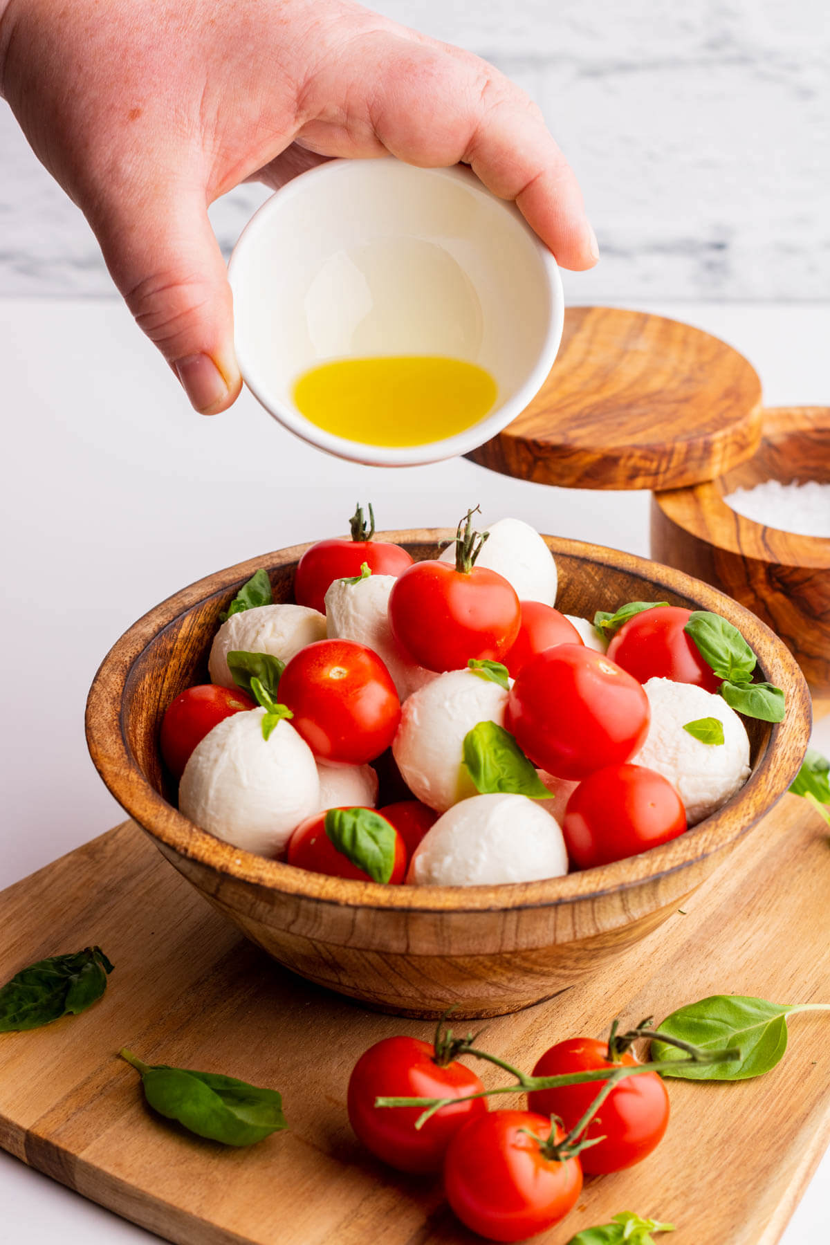 Yellow olive oil being poured over a cherry tomato caprese salad. 