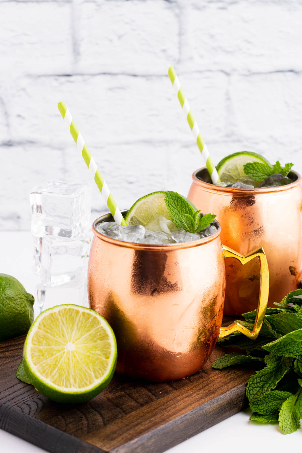 Two icy cocktails in copper mugs surrounded by lime and fresh mint.