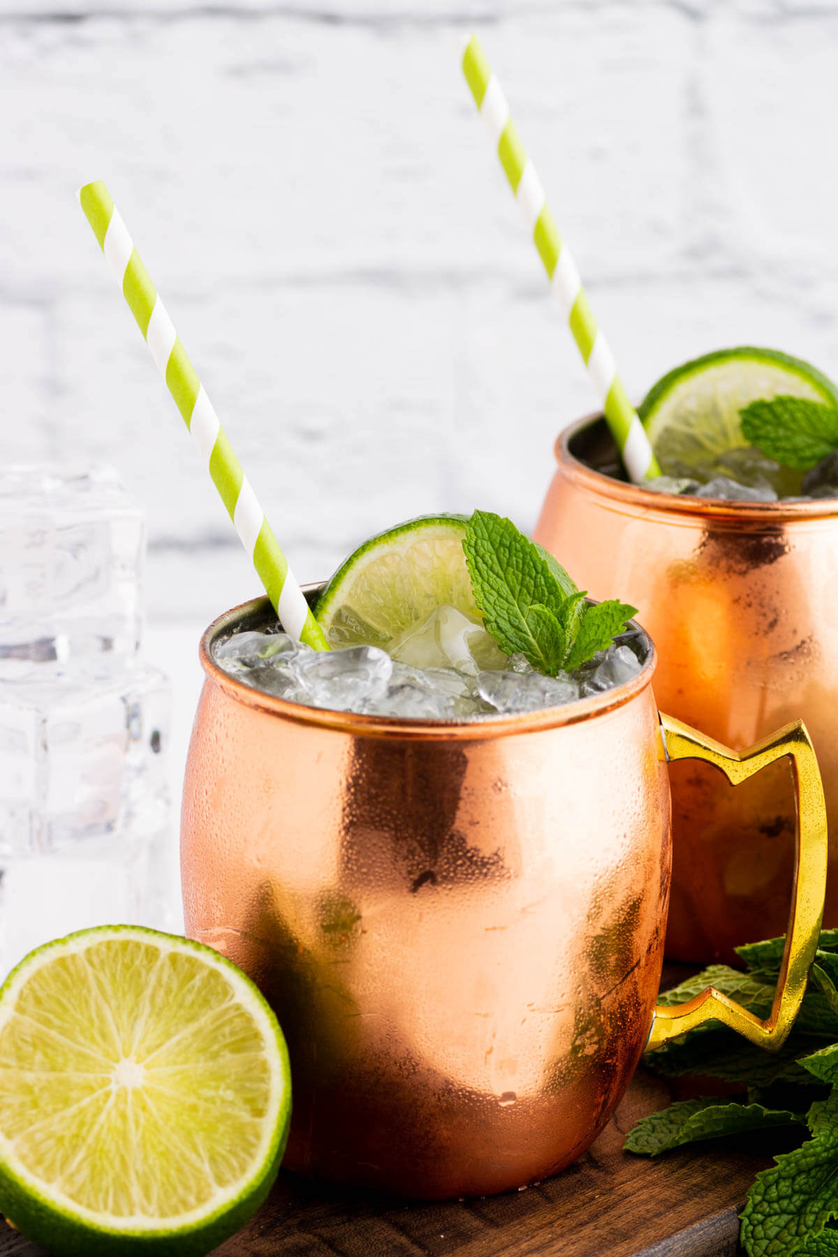 Two icy cocktails in copper mugs surrounded by lime and fresh mint.
